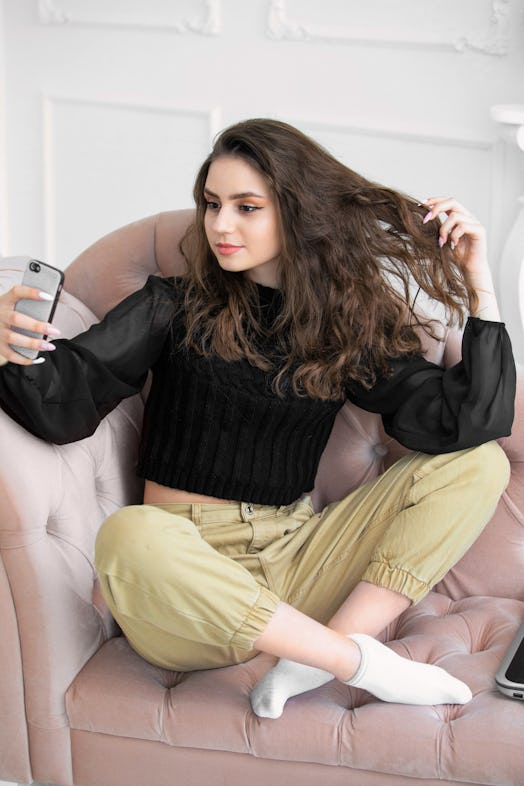 
girl sitting on a sofa in a beautiful setting takes a selfie on a telephon