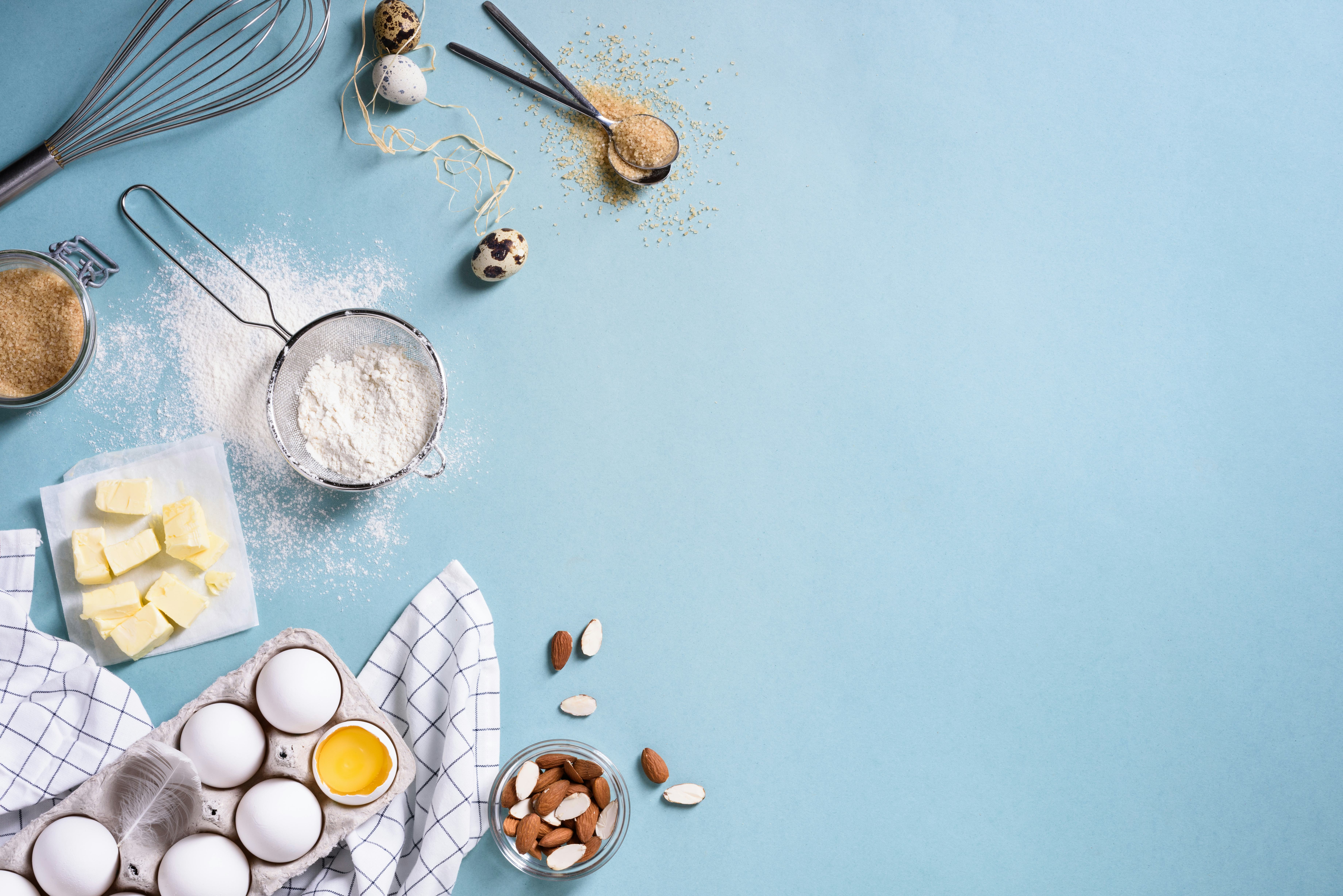 Healthy baking ingredients - flour, almond nuts, butter, eggs, biscuits over a blue table background...