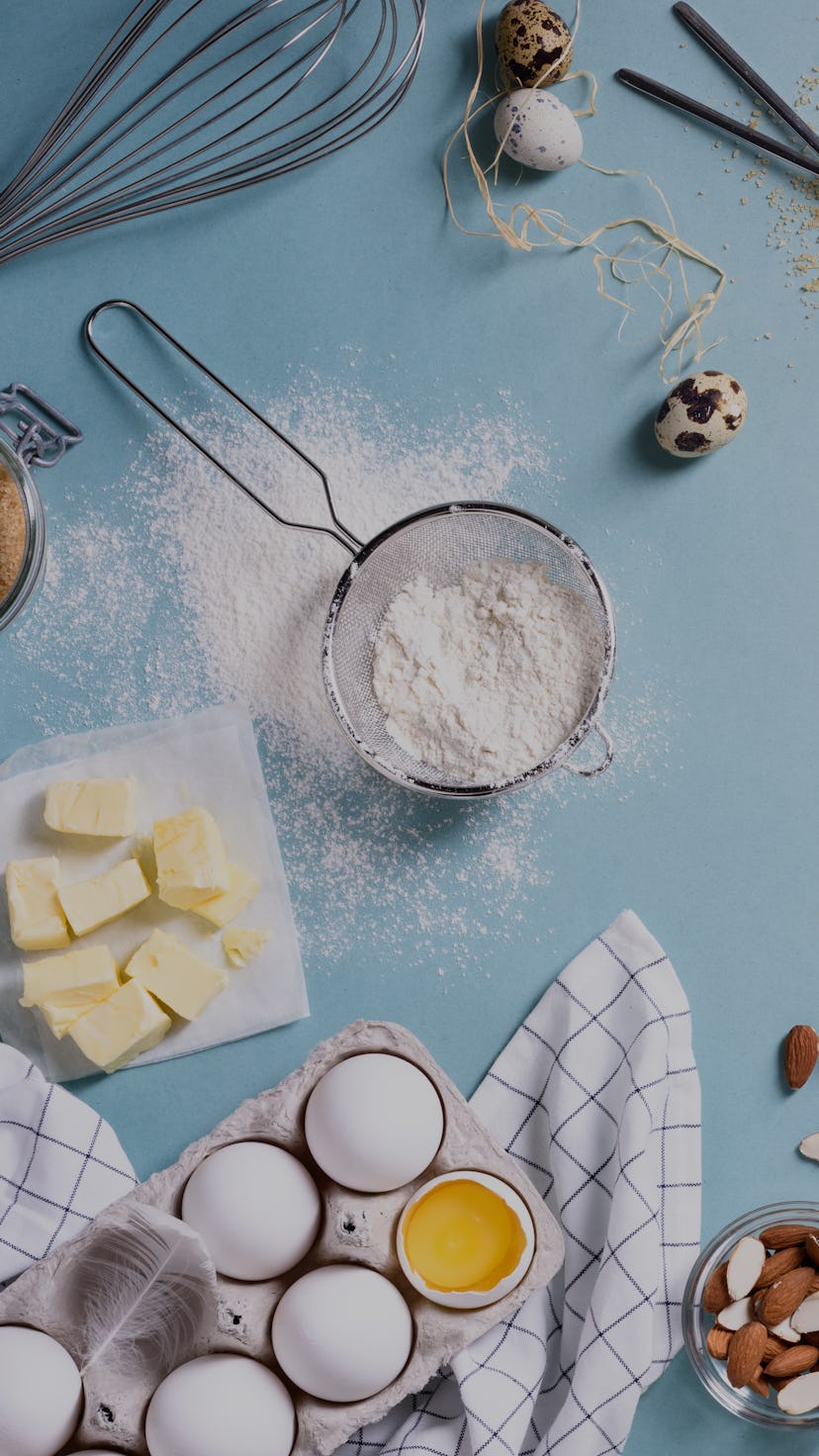 Healthy baking ingredients - flour, almond nuts, butter, eggs, biscuits over a blue table background...