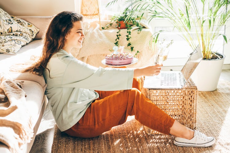 A woman holds her birthday cake while toasting to her friends on the computer.