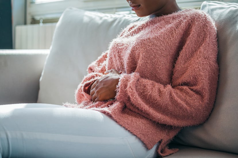 Woman in painful expression holding hands against belly suffering menstrual period pain, lying sad o...