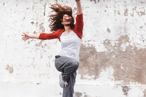 Fitness sport girl in fashion sportswear jumping and dancing hip hop by the street wall, outdoor spo...