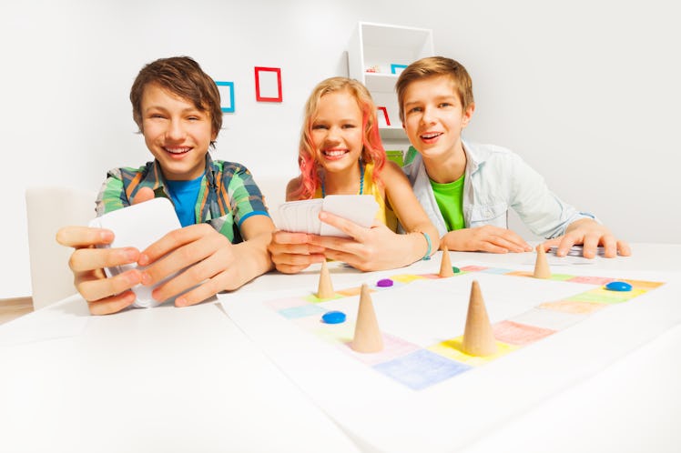 Happy teenagers playing table game holding cards