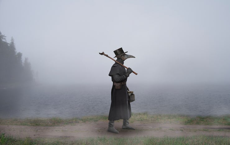 Medieval era. The plague doctor walks along the road near the misty lake