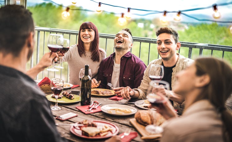 Young friends having fun drinking red wine at balcony penthouse dinner party - Happy people eating b...