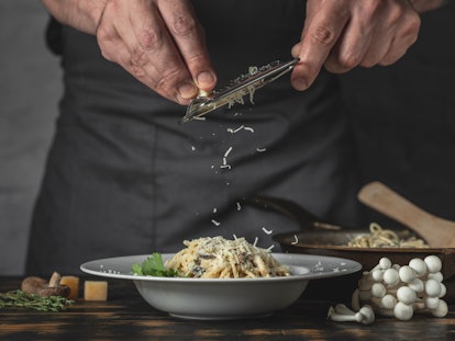 Chef hands cooking Italian pasta and adding cheese parmesan in dish on wooden table background.