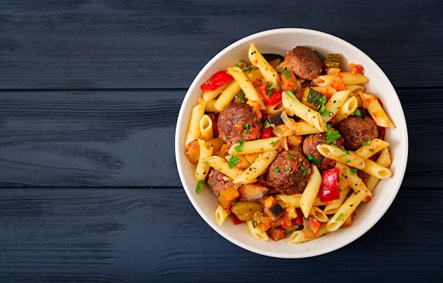 Penne pasta with meatballs in tomato sauce and vegetables in bowl. Top view. Flat lay