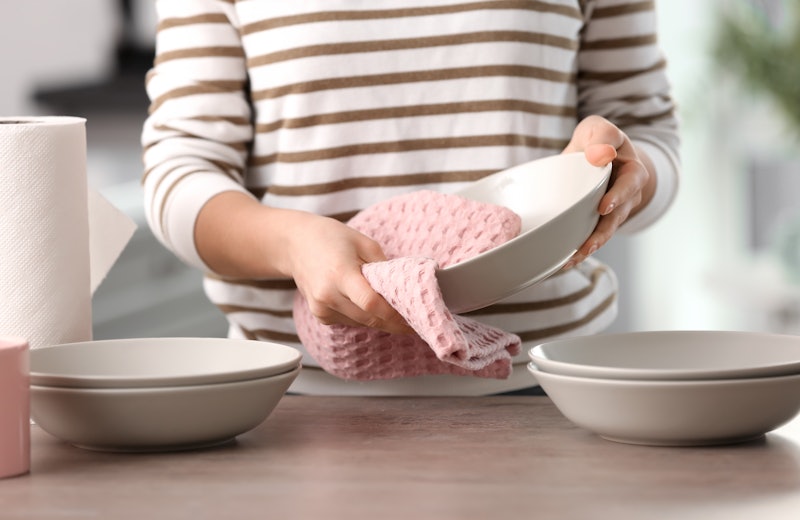 Woman wiping dishware with cotton towel in kitchen