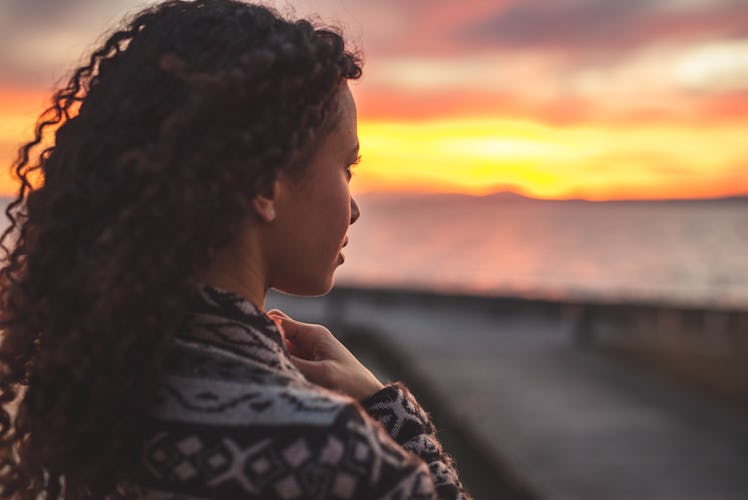 Young African American woman is standing on the promenade at the lake, looking thoughtfully towards ...