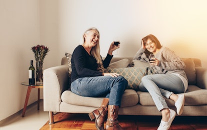 A happy mother and daughter enjoy some wine while sitting on the couch. 