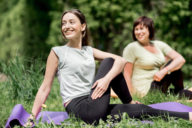 A mother and daughter enjoy doing some yoga outside on the grass.
