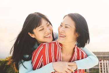 A happy asian mother and daughter smile, look at each other, and hug outside on a sunny day.