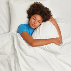 Dark skinned restful woman lying in bed and sleeps peacefully, hugs pillow, enjoys comfort and softn...