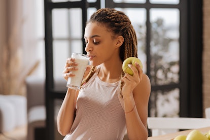 Drinking milk. Appealing fit woman wearing sport top drinking glass of milk and eating green apple