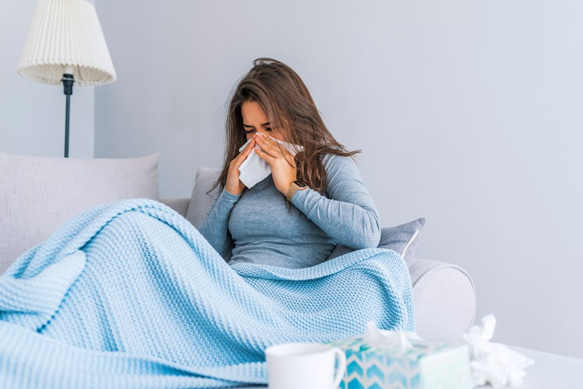 A woman with early signs of lyme disease sitting in bed  blowing her nose while covered with a blue ...