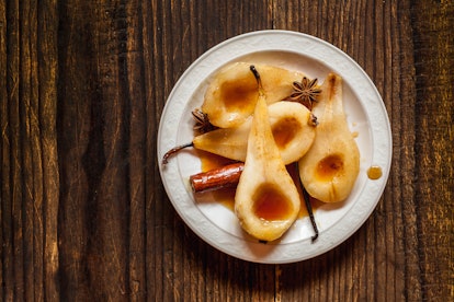Caramelized Pears - Poached pears with spices in syrup on the white plate on a dark wooden table. De...