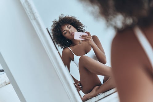 She will melt your heart. Reflection of beautiful young African woman in white lingerie taking selfi...
