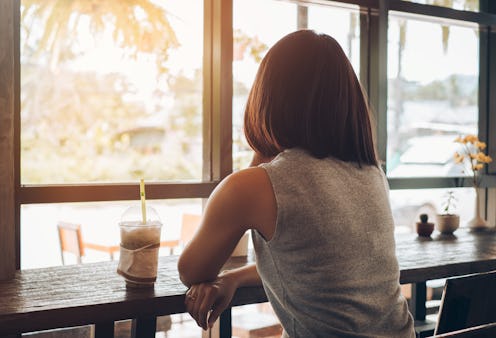 Lonely woman sitting with a cup of coffee in the cafe alone and look at window