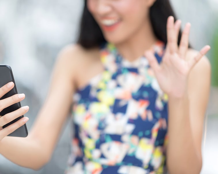Beautiful toothy smiling young woman in white Santa's hat using smartphone doing FaceTime with fami...