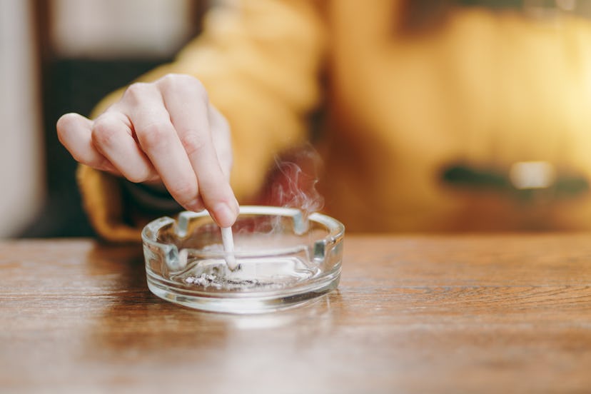 Focus on caucasian young woman hand putting out cigarette on glass ashtray on wooden table, cigarett...