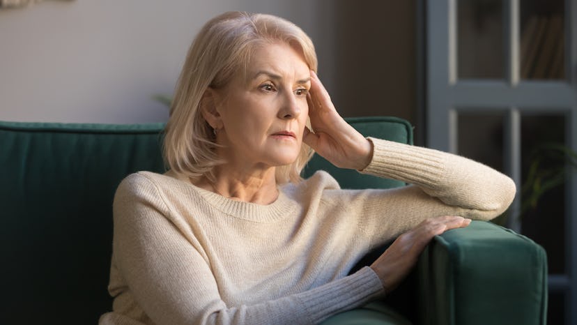 Pensive thoughtful middle-aged lady looking away while sitting on a green couch