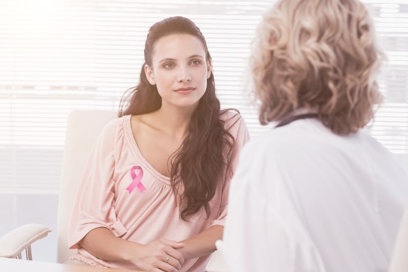 Female patient listening to doctor with concentration in medical office against breast cancer awaren...