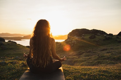 A woman meditates in a field during sunrise.