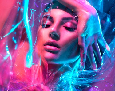 High Fashion model girl in colorful bright neon lights posing in studio through transparent film. Po...