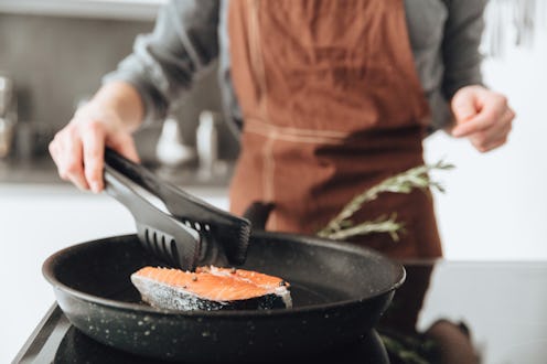 Cropped image of young lady standing in kitchen while cooking fish.