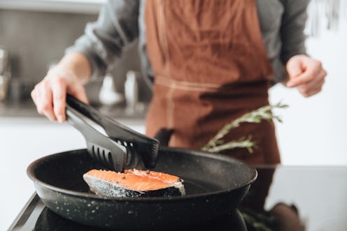 Cropped image of young lady standing in kitchen while cooking fish.