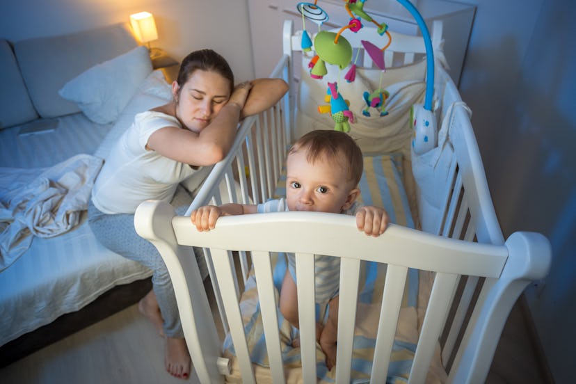 Tired mother falls asleep next to baby's crib