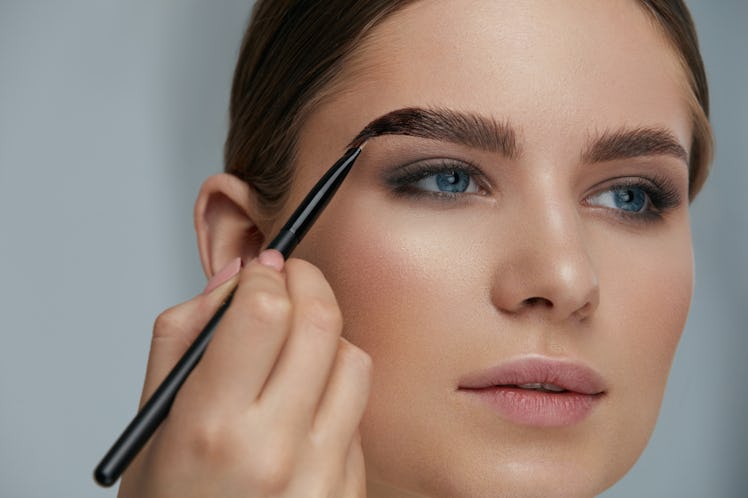 Eyebrow coloring. Woman applying brow tint with makeup brush closeup. Girl model using liquid peel-o...