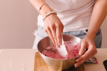 A woman's hands stir a pink dough around in a bowl, in her kitchen. 