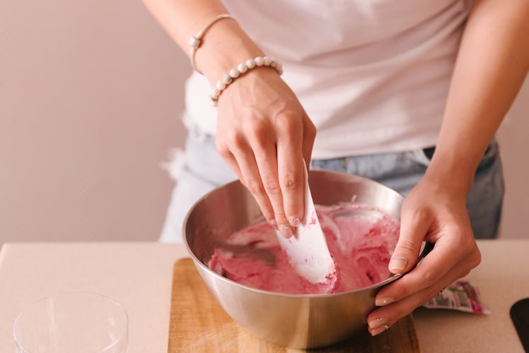 A woman's hands stir a pink dough around in a bowl, in her kitchen.