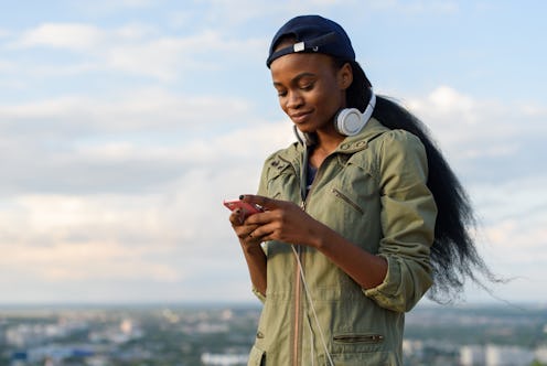 Charming african american girl listen to music and relaxing. Smiling young black lady on blurred cit...