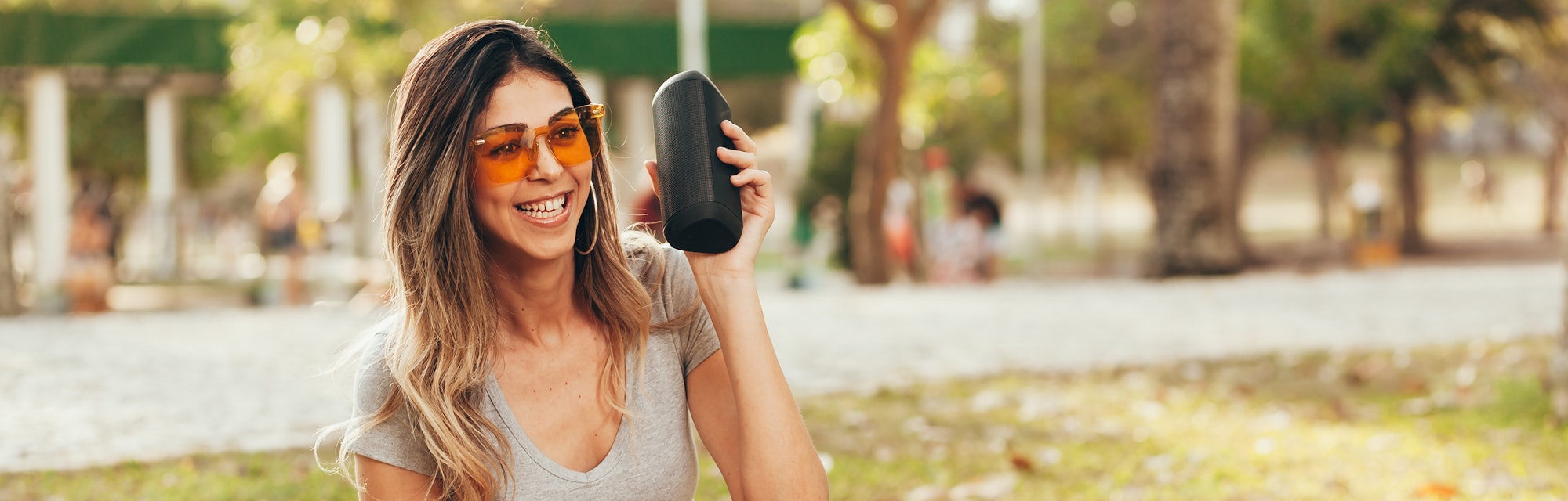Young beautiful woman enjoying the music at outdoor park. Woman listening music by wireless speaker ...