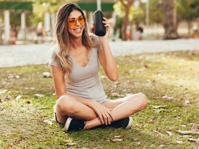 Young beautiful woman enjoying the music at outdoor park. Woman listening music by wireless speaker ...