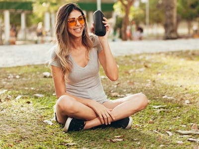 Young beautiful woman enjoying the music at outdoor park. Woman listening music by wireless speaker ...