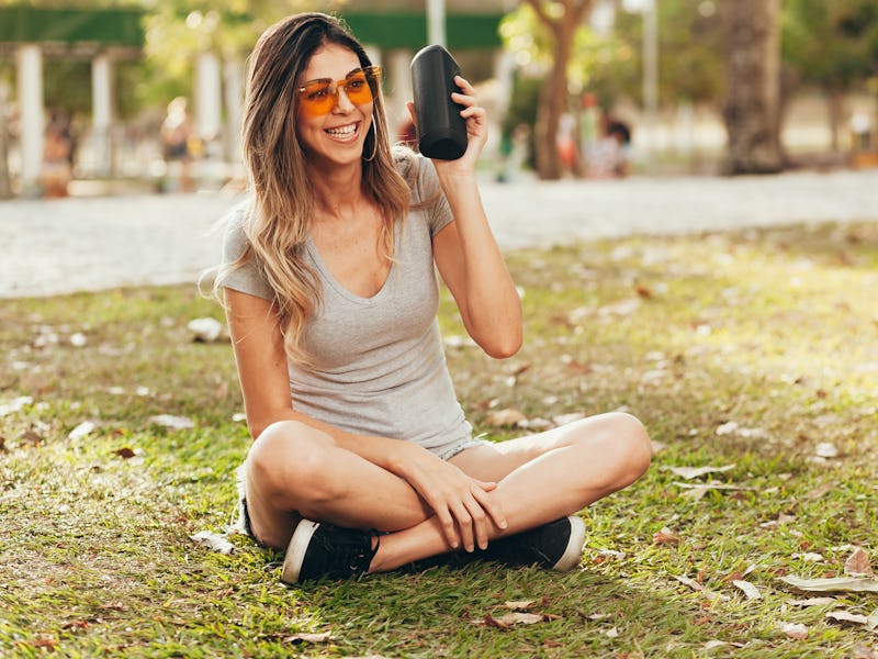 Young beautiful woman enjoying the music at outdoor park. Woman listening music by wireless speaker ...