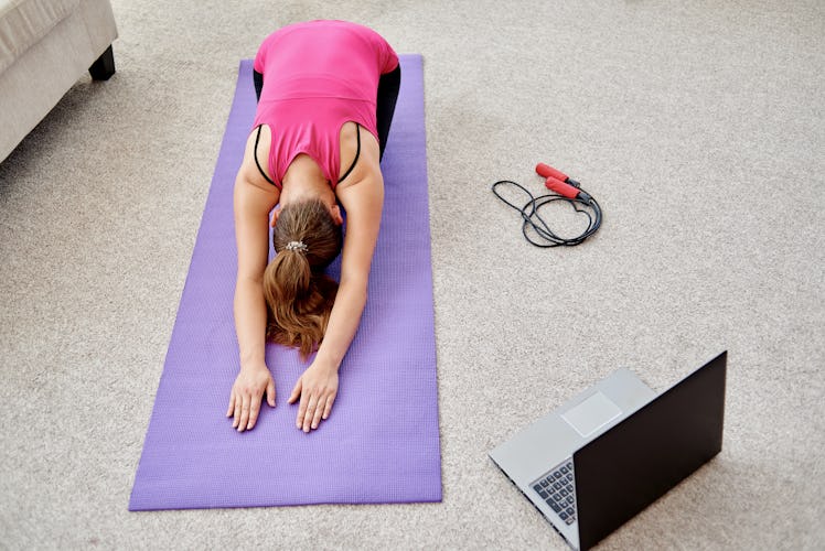 Beautiful young woman doing stretching exercise on floor at home, online training on laptop computer...
