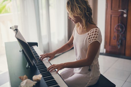 Beautiful woman playing piano inside of house with white curtains.