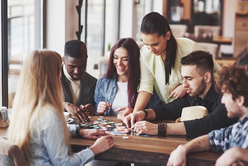 Group of creative friends sitting at wooden table. People having fun while playing board game.