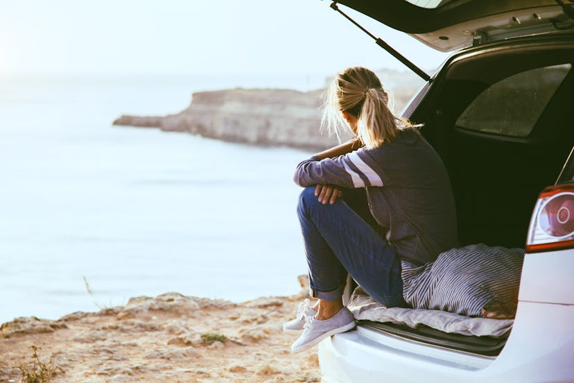 Woman relaxing inside car trunk and watching on sea. Fall trip in sunset. Freedom travel concept. Au...