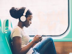 Young black woman listening music travelling by bus using smart phone hand hold, pensive - thoughtfu...