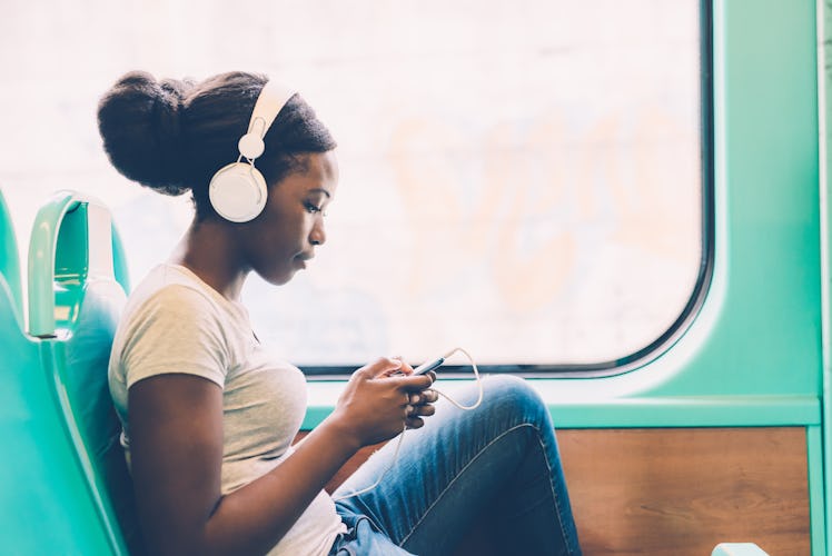 Young black woman listening music travelling by bus using smart phone hand hold, pensive - thoughtfu...