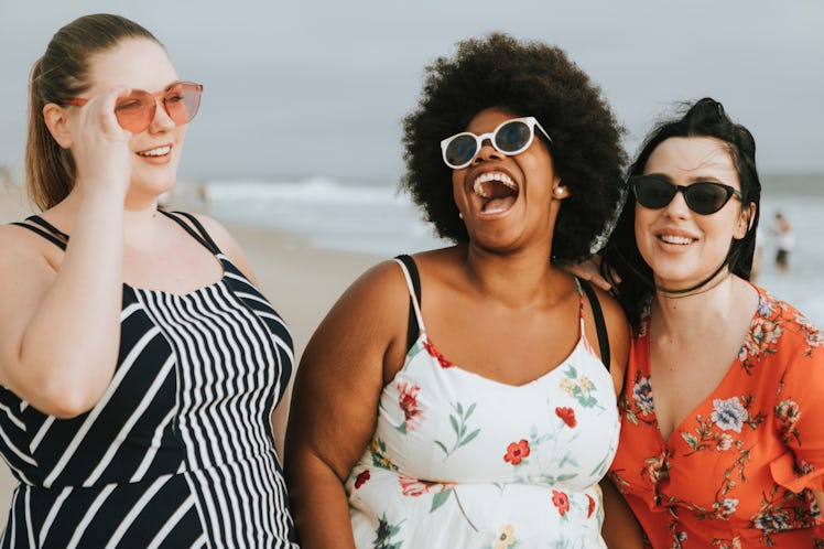Three happy friends laugh while standing on the beach on a summer day.