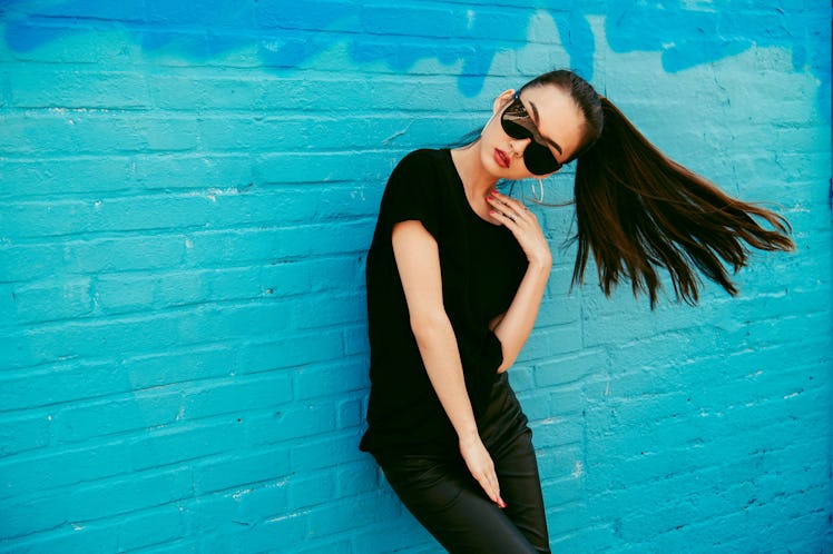 Beautiful young asian girl with long hair wearing sunglasses and black t-shirt posing in front of bl...