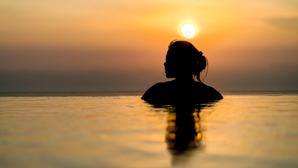 Black silhouette of asian woman on summer vacation holiday relaxing in infinity swimming pool with blue sea sunset view. Healthy happiness lifestyle