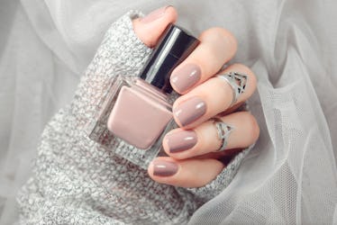 Manicure on female hands with nude nail polish on the grey background.