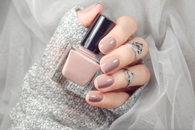 Manicure on female hands with nude nail polish on the grey background.